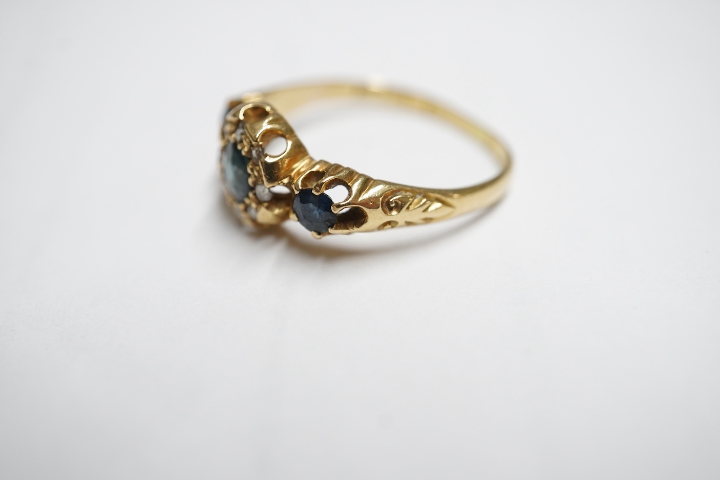 An early 20th century yellow metal and three stone sapphire set half hoop ring, the central stone bordered with rose cut diamonds, size M, gross weight 3 grams.